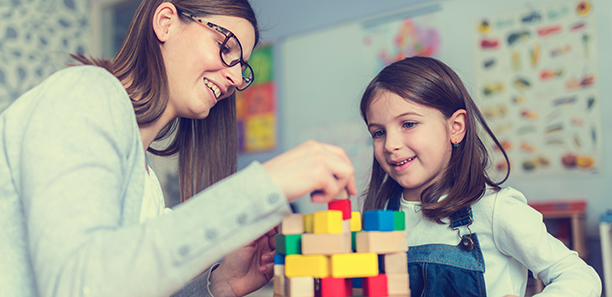 Young child plays with blocks as the teacher helps.