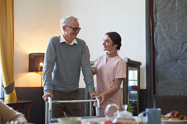 Portrait of smiling young woman helping senior man using walker in nursing home, copy space